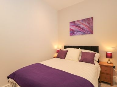 A bedroom with a double bed with purple and white pillows purple throw and bedside tables with lamps at The Nest in North Petherton