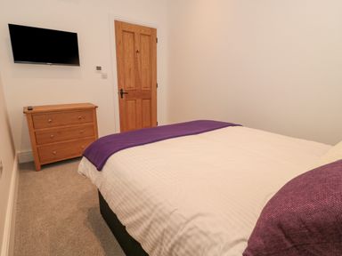 A bedroom with a bed a wooden dresser a wall-mounted television and a wooden door at The Nest in North Petherton