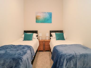 A bedroom with two single beds a bedside table with lamps and a wall painting at The Nest in North Petherton