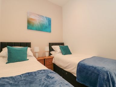 A bedroom with two single beds blue blankets and pillows and a wooden bedside table with lamps at The Nest in North Petherton