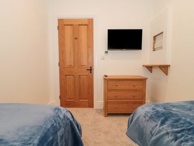 A bedroom with two beds with blue blankets a wooden door a wooden dresser and a wall-mounted television at The Nest in North Petherton