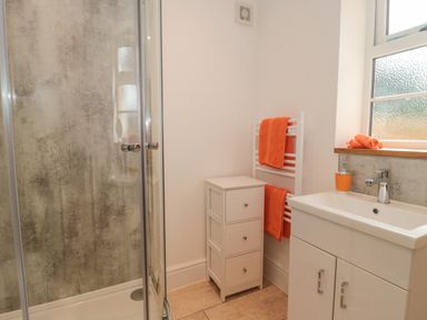 A bathroom with a glass shower enclosure a white cabinet a white sink unit and orange towels at The Nest in North Petherton