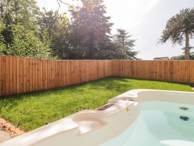 A backyard with a hot tub on a grass lawn surrounded by a wooden fence and trees at The Nest in North Petherton