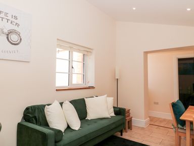 A room with a green sofa and white pillows a wooden dining table with chairs and a window at The Nest in North Petherton