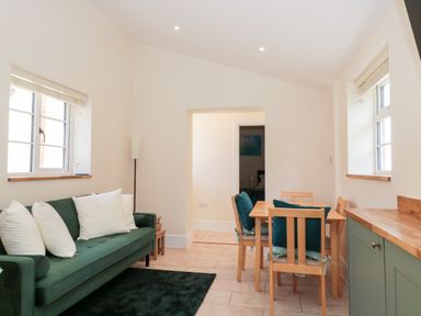 A living room with a green sofa and white cushions next to a wooden dining table with chairs at The Nest in North Petherton