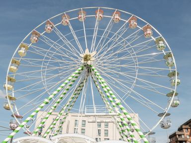 A large ferris wheel with colored cabins and green and white striped supports in an urban area