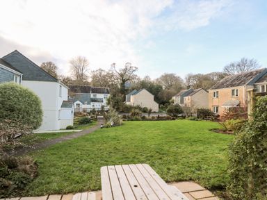A grassy courtyard with bushes and pathways surrounded by houses at Chellowdene Cottage in Falmouth