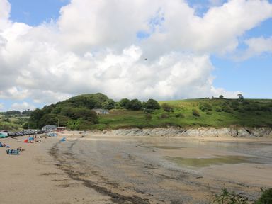 A sandy beach with people and cars near green hills under a partly cloudy sky at Chellowdene Cottage in Falmouth