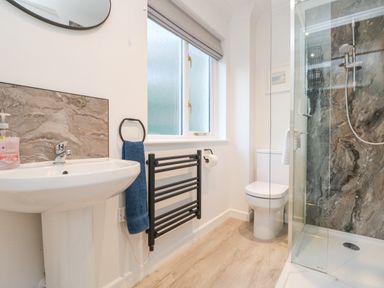 A bathroom with a sink, towel rail, window, toilet, and shower at Chellowdene Cottage in Falmouth