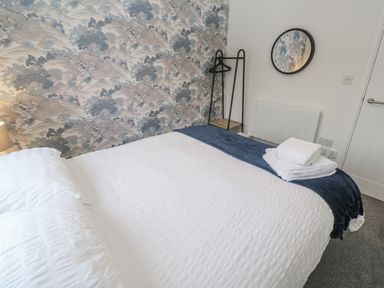 A bedroom with bed, towels, mirror and lamp at Chellowdene Cottage in Falmouth