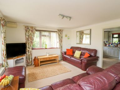 A living room with leather sofas a wooden coffee table a television and a window with patterned curtains at The Clove in Poyston Cross near Haverfordwest