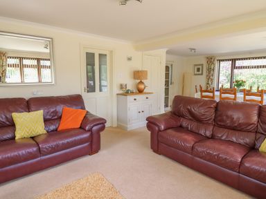 A living room with two brown leather sofas a white cabinet with a lamp and a dining area with a wooden table and chairs at The Clove in Poyston Cross near Haverfordwest