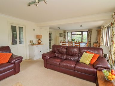 A living room with leather sofas and a wooden dining table near windows at The Clove in Poyston Cross near Haverfordwest