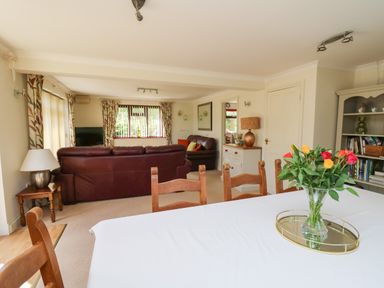A dining area with a table and chairs and a vase of flowers next to a living room with sofas and a lamp at The Clove Poyston Cross near Haverfordwest