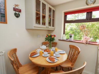 A kitchen dining area with a wooden round table set with croissants orange juice cups and a teapot near a window at The Clove in Poyston Cross near Haverfordwest