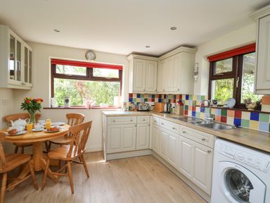 A kitchen with white cabinets wooden table and chairs set for breakfast at The Clove in Poyston Cross near Haverfordwest