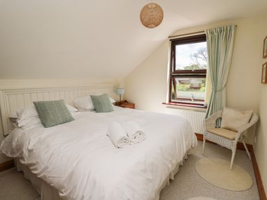A bedroom with a double bed two green pillows a wicker chair near a window at The Clove in Poyston Cross near Haverfordwest