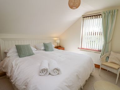 A bedroom with a double bed two green pillows rolled towels bedside table lamp window with curtains and a wicker chair at The Clove in Poyston Cross near Haverfordwest