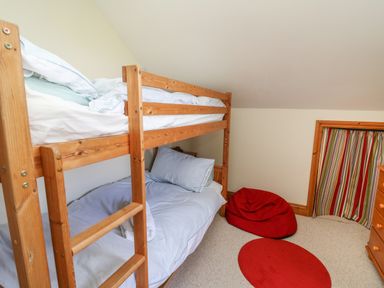 A bedroom with wooden bunk beds red bean bag and striped curtains at The Clove in Poyston Cross near Haverfordwest