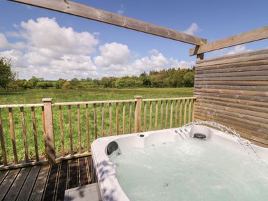 An outdoor hot tub on a wooden deck with a railing overlooking a grassy field and trees at The Clove in Poyston Cross near Haverfordwest