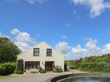A building with windows and a bench outside near a round pond and greenery at The Clove in Poyston Cross near Haverfordwest