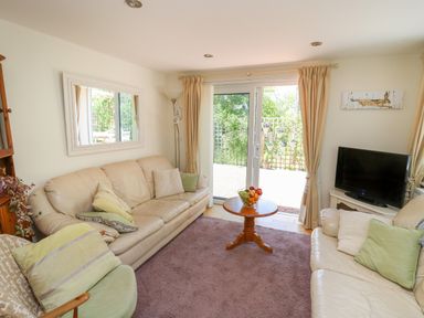 A living room with beige sofas a round wooden table with fruit and sliding glass doors at Lavender Lodge in Haverfordwest