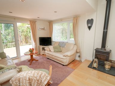 A living room with cream sofas a wooden coffee table a television and a wood burning stove at Lavender Lodge in Haverfordwest