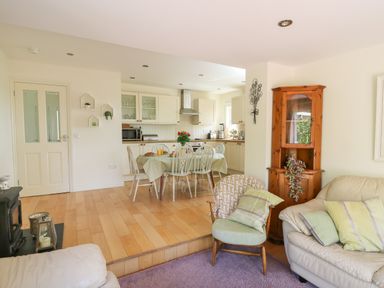 An open plan living area with a kitchen dining table and chairs a wooden cabinet and armchairs at Lavender Lodge in Haverfordwest