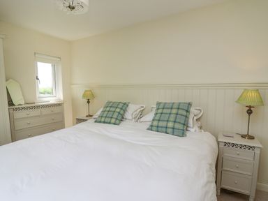 A bedroom with a large bed two plaid pillows two bedside tables with lamps and a dresser with a mirror at Lavender Lodge in Haverfordwest