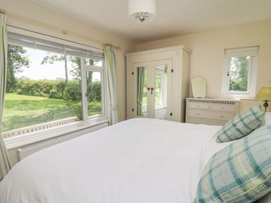 A bedroom with a large bed with pillows next to a window showing a grassy garden and white wardrobe with mirrors and a dresser with a mirror at Lavender Lodge in Haverfordwest