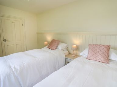 A bedroom with two single beds white bedding pink pillows bedside table with lamps and a closed door at Lavender Lodge in Haverfordwest