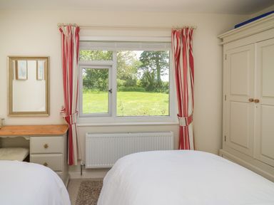 A bedroom with two beds a window with red and white curtains a radiator a wardrobe and a desk at Lavender Lodge in Haverfordwest