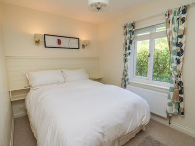 A bedroom with a double bed white bedding wall lamps and a window with patterned curtains at Lavender Lodge in Haverfordwest