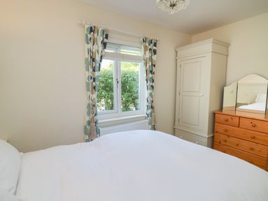 A bedroom with a bed a window with patterned curtains a white wardrobe and a wooden dresser with a mirror at Lavender Lodge in Haverfordwest