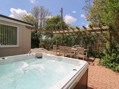 An outdoor patio with a hot tub and wooden seating under a pergola surrounded by plants at Lavender Lodge in Haverfordwest