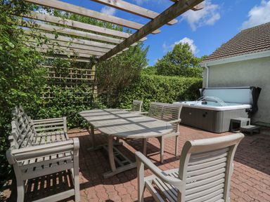 An outdoor patio with wooden table and chairs under a pergola next to a hot tub at Lavender Lodge in Haverfordwest