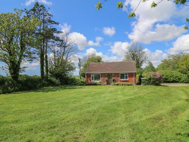 A single-story brick house with a front lawn and trees under a blue sky at Lavender Lodge in Haverfordwest