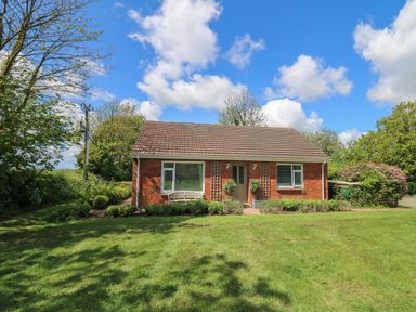 A brick bungalow with a tiled roof fronted by a lawn and shrubs at Lavender Lodge in Haverfordwest