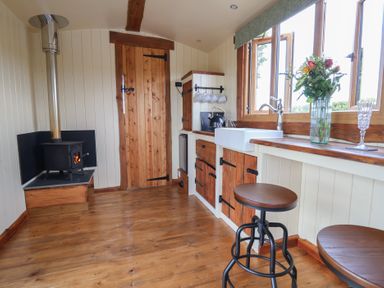 A kitchen with wooden floor and cabinets a small stove and a window with flowers at The Coop in Aston near Woore