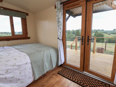A bedroom with a bed near wooden framed glass doors leading to a deck at The Coop in Aston near Woore