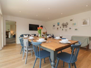 A dining room with a wooden table set with bowls and glasses and blue chairs at Little Chapter in Walberswick