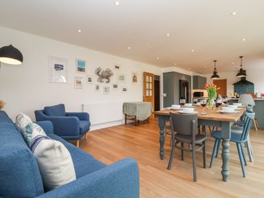 A living area with blue sofas and a wooden dining table set with dishes and glasses at Little Chapter in Walberswick
