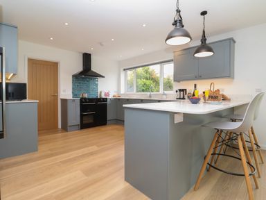 A kitchen with a large island bar with stools under hanging lights and cabinets at Little Chapter in Walberswick