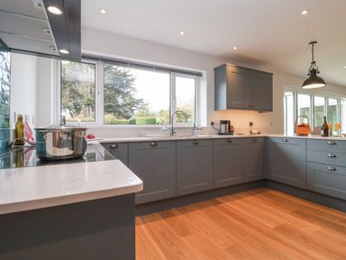 A kitchen with gray cabinets a pot on the stove and a window overlooking trees at Little Chapter in Walberswick