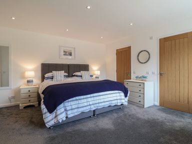 A bedroom with a double bed bedside tables lamps a dresser and two wooden doors at Little Chapter in Walberswick