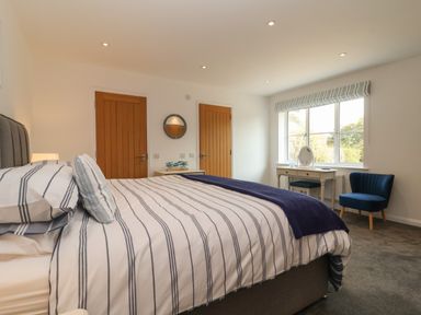 A bedroom with a striped bed, wooden doors, a desk under a window, and a blue chair at Little Chapter in Walberswick