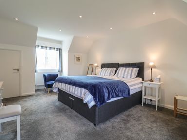A bedroom with a large bed blue blanket bedside tables lamps a chair and a window at Little Chapter in Walberswick