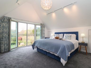 A bedroom with a blue bedspread curtains and two bedside tables with lamps at Little Chapter in Walberswick