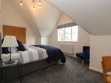 A bedroom with a bed with striped bedding a blue chair a window with a roman blind and a wooden door at Little Chapter in Walberswick