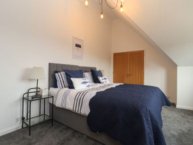 A bedroom with a double bed with blue and white bedding two bedside tables with lamps and a wooden wardrobe at Little Chapter in Walberswick